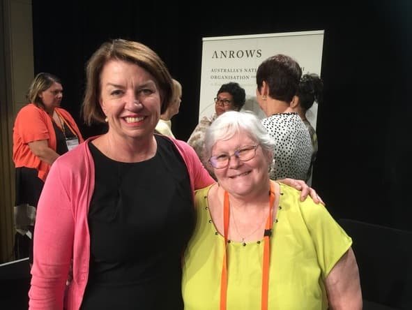Two women smiling together at the conference, an ANROWS banner behind them.