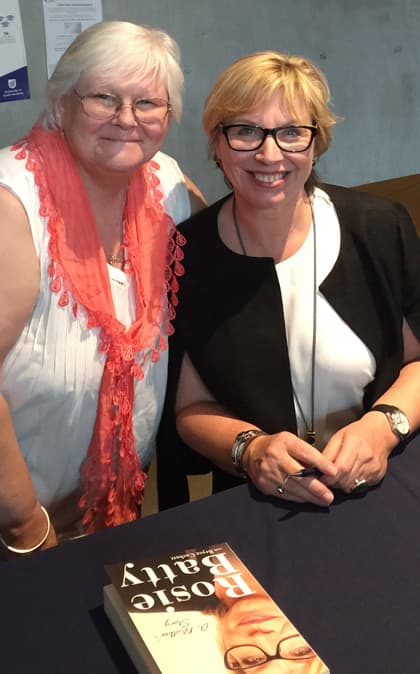 Glyn Scott standing beside Rosie Batty, who is seated at a table signing copies of her book, A Mother's Story.